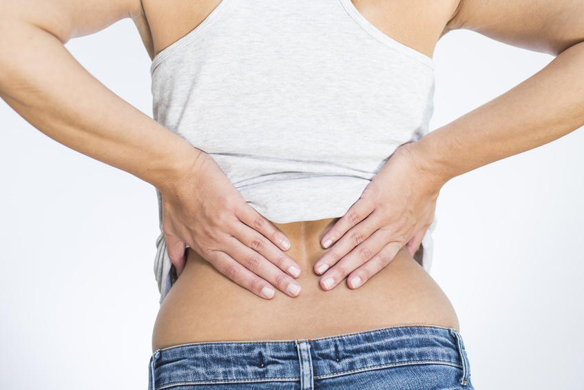Rear view of a woman with lower back pain clutching her hands to her back and spine to relieve the ache in her muscles or spinal vertebrae and discs brought on by stress, injury or disease